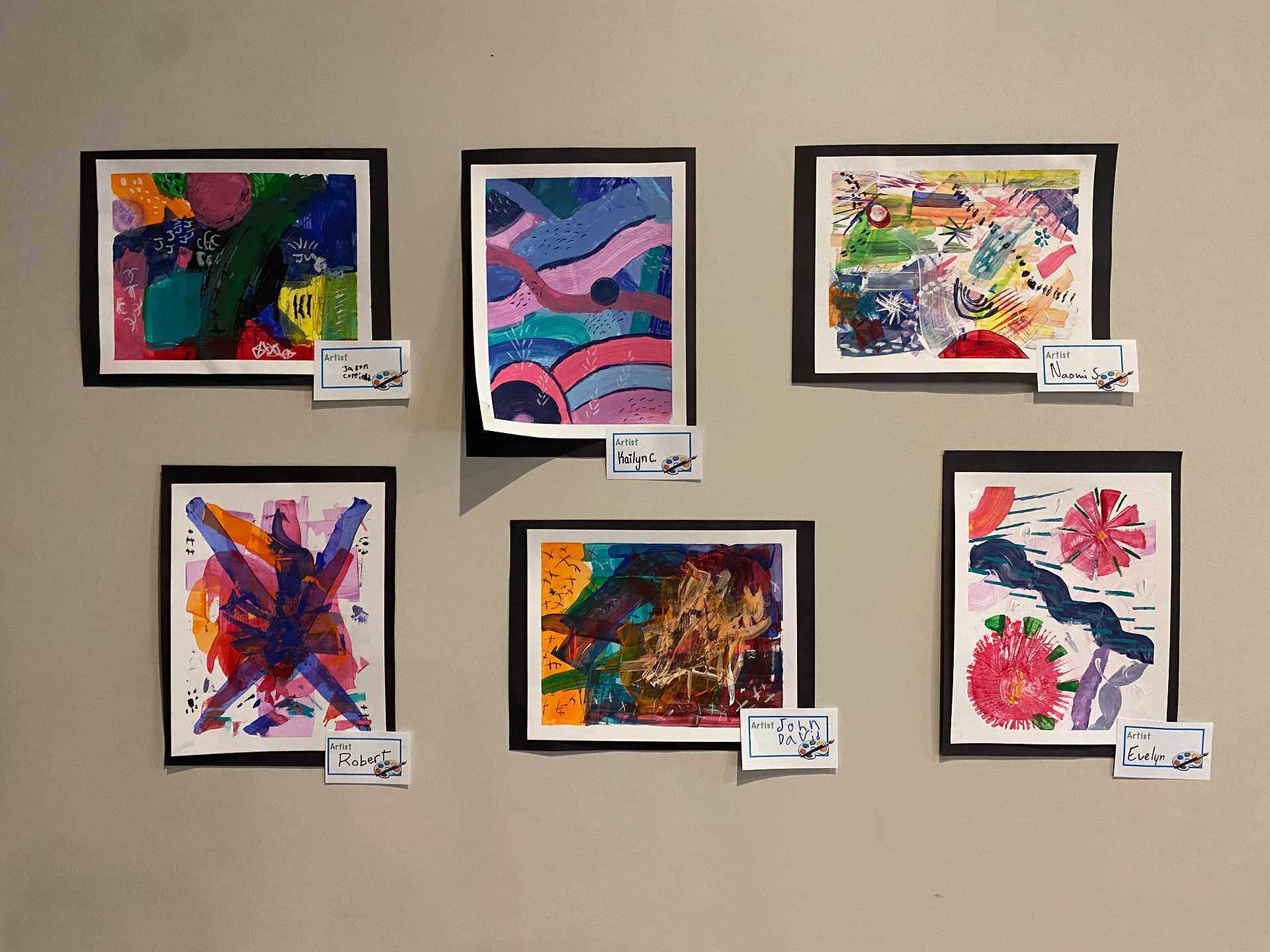 A wall display of children's vibrant abstract paintings